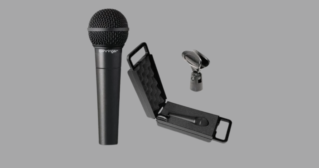 O kit completo do microfone Behringer XM8500, exibindo o microfone, o estojo rígido de transporte forrado com espuma e o cachimbo para pedestal inclusos na caixa.