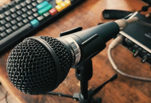 Close-up do microfone dinâmico Behringer XM8500 em um pedestal, destacando sua construção robusta em metal e a grade prateada, representando um áudio profissional com excelente custo-benefício.