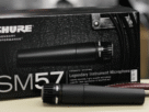 Close do icônico microfone dinâmico Shure SM57, detalhando sua grade prateada e design robusto, pronto para uso em estúdio ou palco.