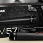 Close do icônico microfone dinâmico Shure SM57, detalhando sua grade prateada e design robusto, pronto para uso em estúdio ou palco.