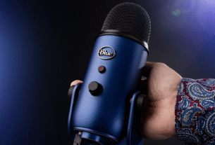 O microfone USB condensador Blue Yeti em seu design prateado icônico, sobre seu pedestal de mesa pesado, em um artigo de review.