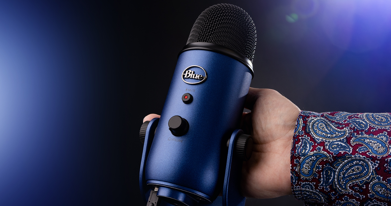 O microfone USB condensador Blue Yeti em seu design prateado icônico, sobre seu pedestal de mesa pesado, em um artigo de review.