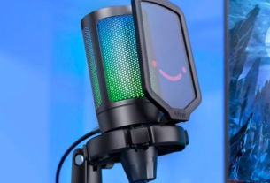Microfone Fifine A6V com iluminação RGB ativa em um setup gamer moderno, destacando seu design compacto, filtro pop e suporte shock mount para streaming e podcasts.