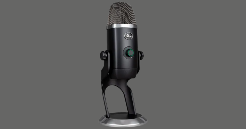 Close-up do microfone USB Blue Yeti em sua base de mesa padrão, evidenciando sua construção metálica e os controles físicos de ganho e padrões polares para gravações versáteis.