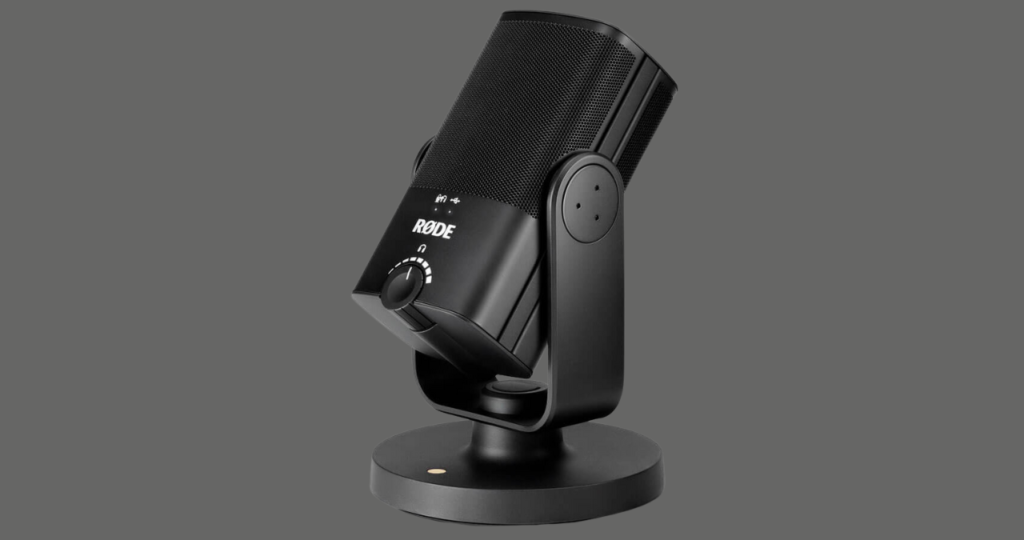 O microfone condensador Rode NT-USB posicionado em sua base de mesa ao lado de um laptop, ilustrando uma configuração simples e prática de microfone USB para gravar podcasts em casa.