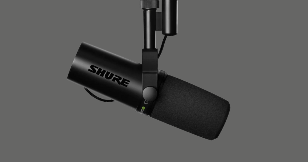 Microfone dinâmico Shure SM7B preto montado em um suporte articulado em um estúdio de rádio, destacando seu design clássico e robusto utilizado por podcasters profissionais.