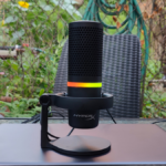 Microfone condensador USB HyperX DuoCast com anel de iluminação RGB colorido ativo, posicionado em um setup profissional de streaming e podcast.