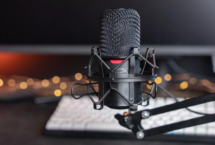 Microfone condensador USB HyperX SoloCast em cor preta, posicionado em seu pedestal de mesa original em um setup de escritório moderno e minimalista.