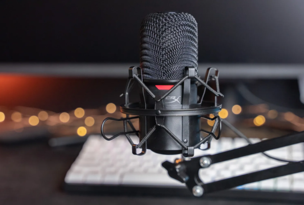 Microfone condensador USB HyperX SoloCast em cor preta, posicionado em seu pedestal de mesa original em um setup de escritório moderno e minimalista.