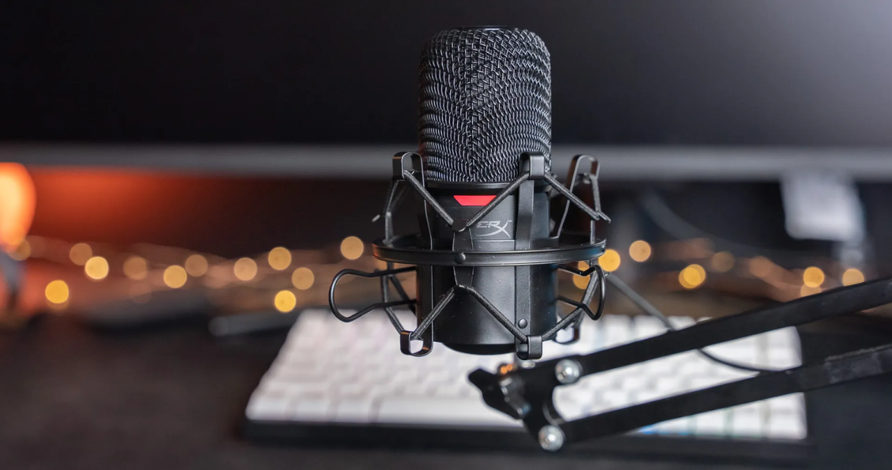 Microfone condensador USB HyperX SoloCast em cor preta, posicionado em seu pedestal de mesa original em um setup de escritório moderno e minimalista.