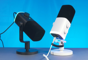 Microfone dinâmico Fifine Ampligame AM9 com design retangular moderno e anel de iluminação RGB, posicionado em um setup de streaming profissional.